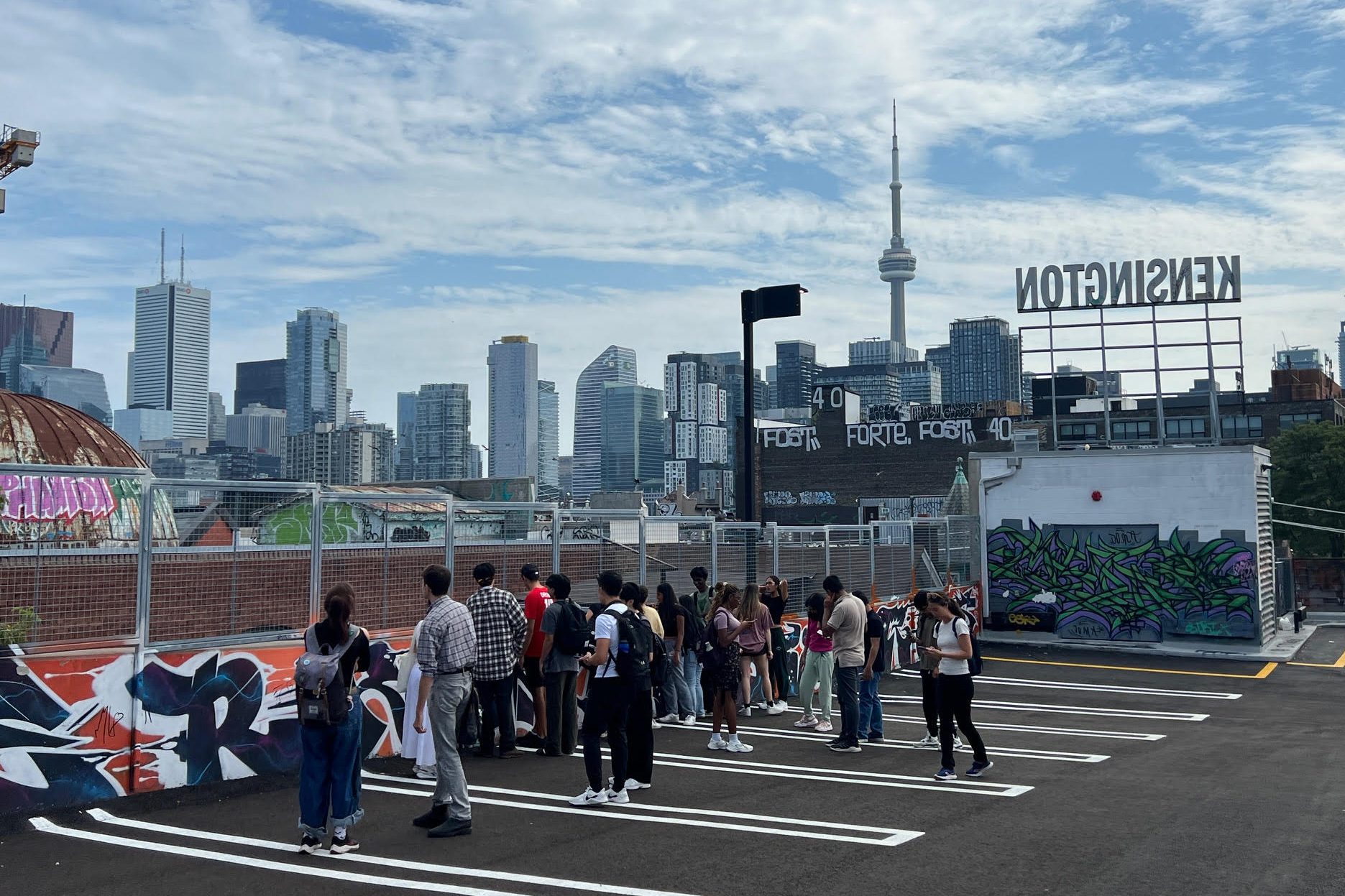 A group of students stands on the roof of a parking garage with a "KENSINGTON" sign and the CN Tower in the background