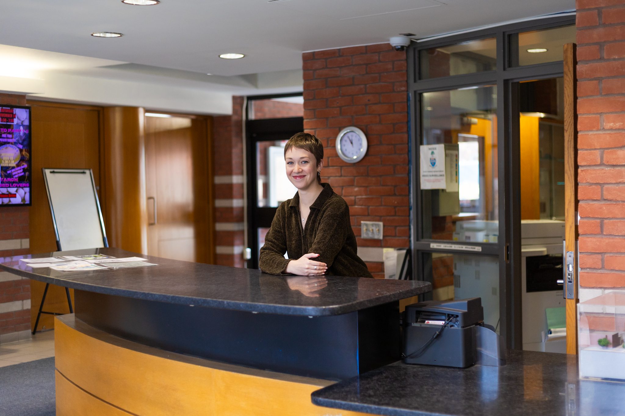 residence steward, Riley Myers, stands behind a lobby reception desk smiling