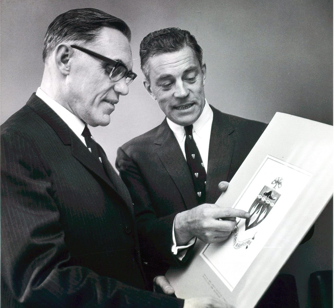 Two men looking at a picture of the newly-designed Innis College crest