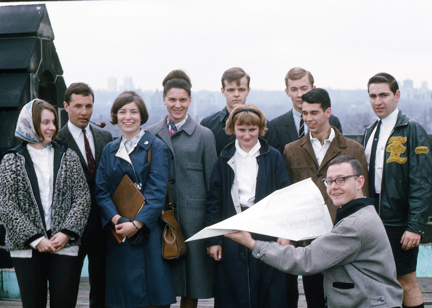 Smiling people posing for a photo, one person in front holding a large exam timetable folded into a paper airplane