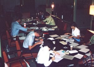 Many people sitting at a large table writing letters to incoming students.