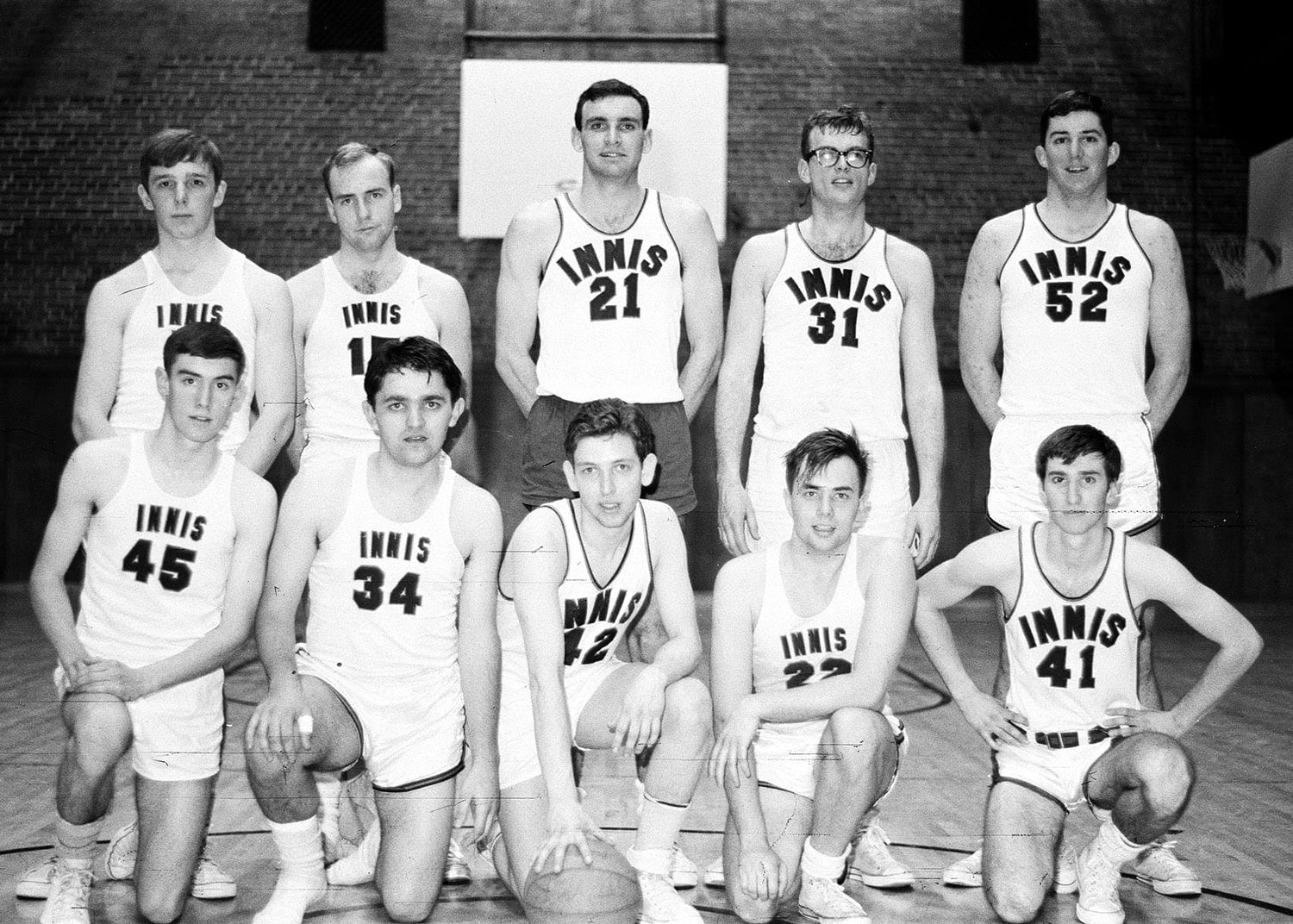 Black and white photo of the Men's Intramural Basketball Team posing wearing their uniforms.