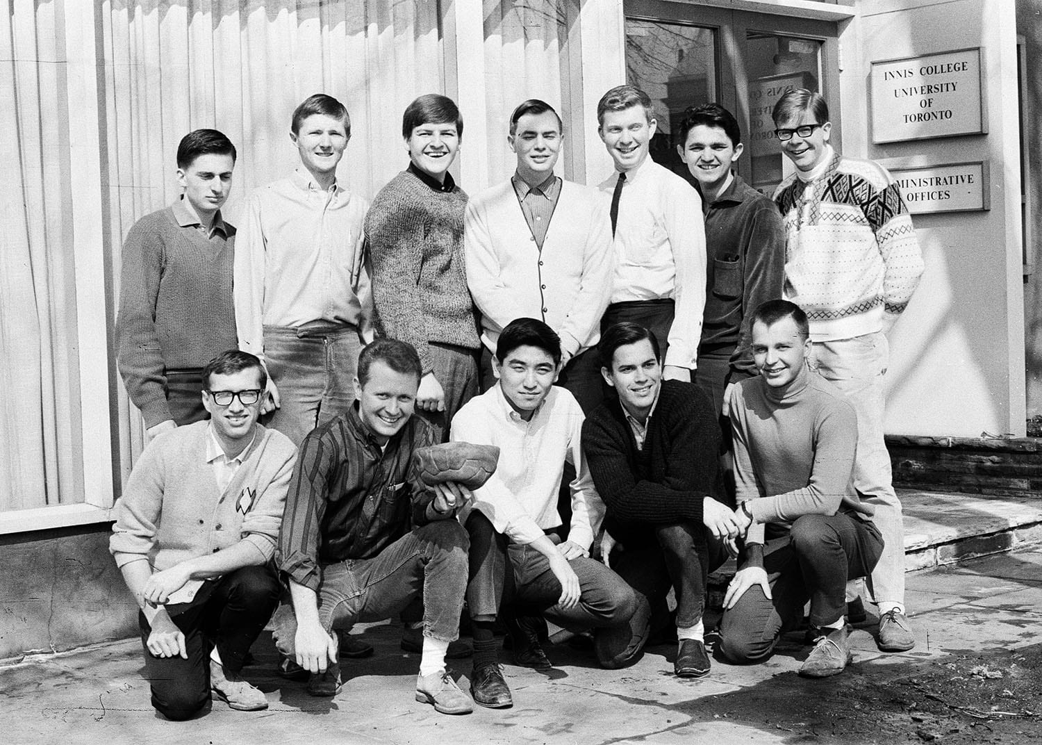 Men's Soccer team posing for a photo outside the Innis College Administrative Offices. One man is holding a deflated soccer ball.