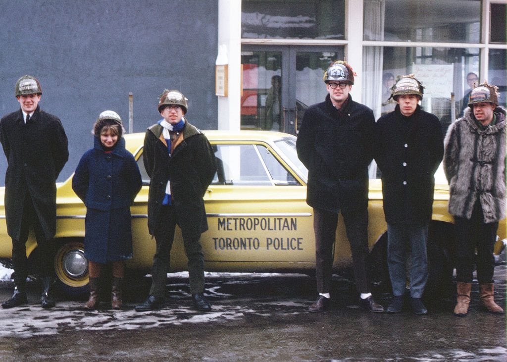 Group of people in home-made helmets standing in front of a yellow Metropolitan Toronto Police car